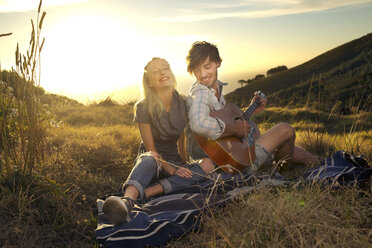 Glückliches junges Paar mit Gitarre auf einer Decke auf einer Wiese - TOYF000600
