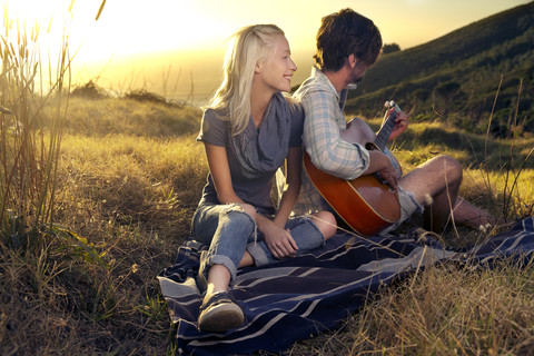 Junges Paar mit Gitarre auf einer Decke auf einer Wiese, lizenzfreies Stockfoto