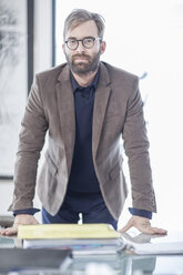 Businessman standing at desk looking to camera - ZEF005735