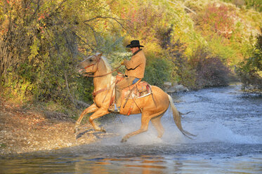 USA, Wyoming, Cowboy reitet auf seinem Pferd über den Fluss - RUEF001588