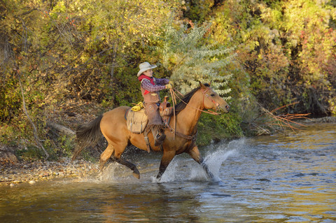 USA, Wyoming, junger Cowboy reitet auf seinem Pferd über den Fluss, lizenzfreies Stockfoto
