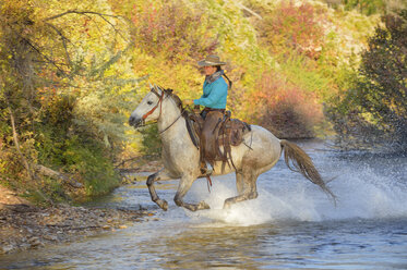 USA, Wyoming, cowgirl riding his horse across river - RUEF001590