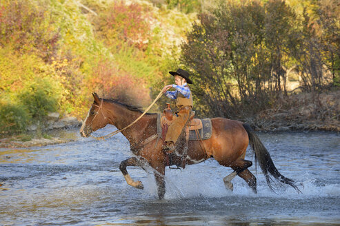 USA, Wyoming, young cowboy riding his horse across river - RUEF001592