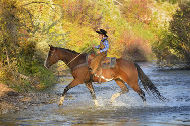USA, Wyoming, junger Cowboy reitet auf seinem Pferd über den Fluss - RUEF001593