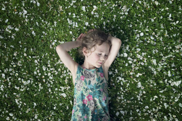 Little girl lying on meadow with scattered apple blossoms - OPF000057