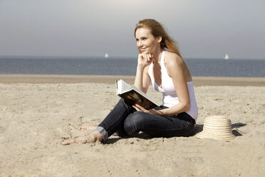 Netherlands, Scheveningen, young woman with book sitting on sandy beach - GDF000725