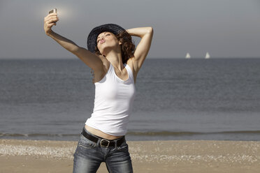 Netherlands, Scheveningen, young woman taking a selfie on the beach - GDF000724