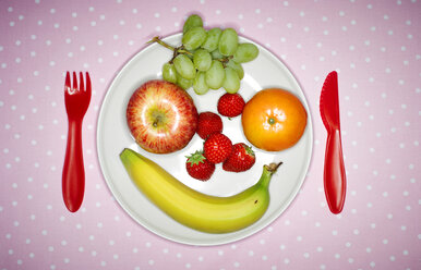 Plate with fruits building funny face and red plastic cutlery on pink cloth - KSWF001508