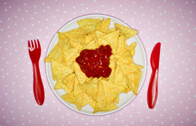 Plate of cheese nachos with salsa and red plastic cutlery on pink cloth - KSWF001511