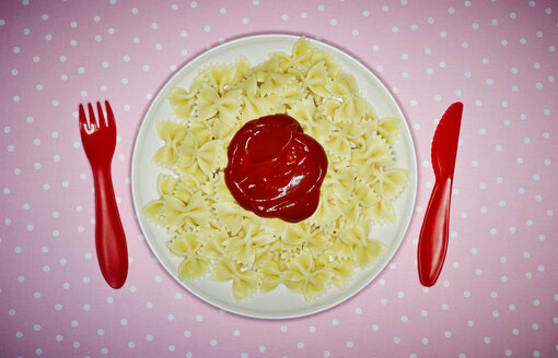 Plate of Farfalle with ketchup and red plastic cutlery on pink cloth - KSWF001516