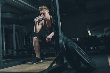 Junger Mann trinkt Wasser im Fitnessstudio - MADF000314