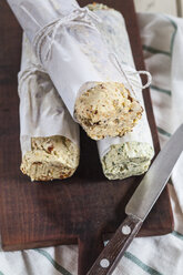 Three rolls of differently flavoured compound butters on chopping board - SBDF001873