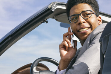 Young black man sitting in convertible, talking on the phone - ABZF000051