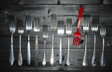 Row of different silver forks and a red plastic fork on wood - KSWF001523