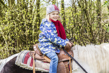 Porträt eines lächelnden kleinen Mädchens, das auf einem Pony sitzt - JFEF000656