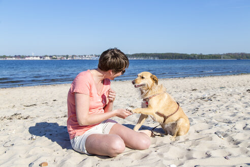 Deutschland, Kiel, Frau sitzt mit ihrem Hund am Sandstrand - JFEF000672
