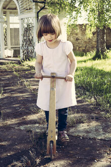 Little girl with old wooden scooter in a garden - LVF003389