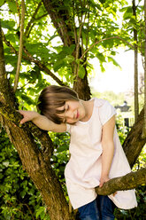 Porträt eines lächelnden kleinen Mädchens mit geschlossenen Augen, das auf einem Ast sitzt - LVF003393
