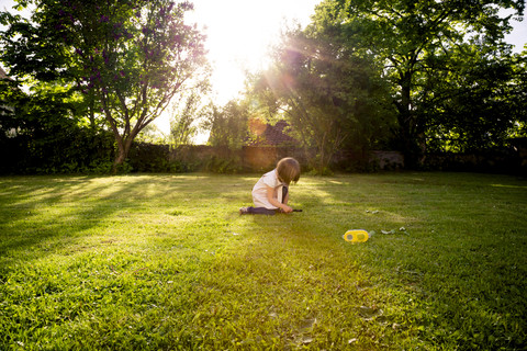 Kleines Mädchen hockt auf einer Wiese und benutzt ein Vergrößerungsglas, lizenzfreies Stockfoto