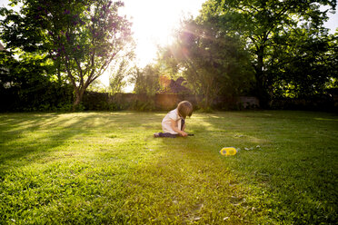 Little girl crouching on a meadow using magnifying glass - LVF003396