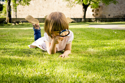 Little girl lying on a meadow using magnifying glass - LVF003402