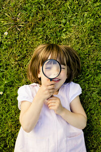 Little girl lying on a meadow looking through magnifying glass - LVF003403