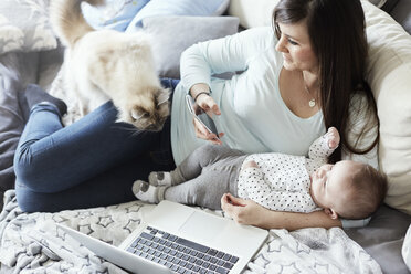 Junge Mutter und Baby auf der Couch liegend mit Katze und Laptop - STKF001275