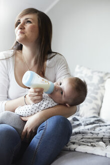 Junge Mutter, die ihr Baby zu Hause mit der Flasche füttert - STKF001244