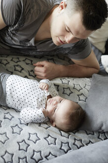 Young father lying on couch looking at baby - STKF001250