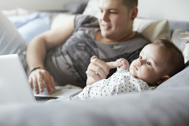 Junger Vater mit Laptop und Baby auf der Couch liegend - STKF001255
