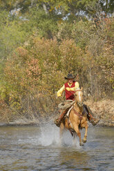 USA, Wyoming, Cowboy reitet auf seinem Pferd über den Fluss - RUEF001598