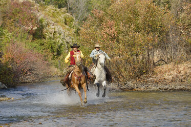 USA, Wyoming, Cowboy und Cowgirl reiten auf ihren Pferden über den Fluss - RUEF001599