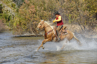 USA, Wyoming, Cowboy reitet auf seinem Pferd über den Fluss - RUEF001600