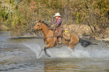 USA, Wyoming, Junger Cowboy reitet auf seinem Pferd über den Fluss - RUEF001601