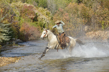 USA, Wyoming, Cowgirl reitet auf ihrem Pferd über den Fluss - RUEF001602