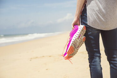 Portugal, Faro, woman on the beach holding pink sneakers in her hand - CHPF000144