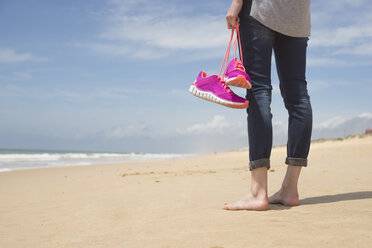 Portugal, Faro, barfuß Frau am Strand trägt ihre rosa Turnschuhe - CHPF000143