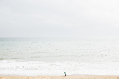 Spanien, Mallorca, Eine Person mit Regenschirm geht am Strand entlang, lizenzfreies Stockfoto