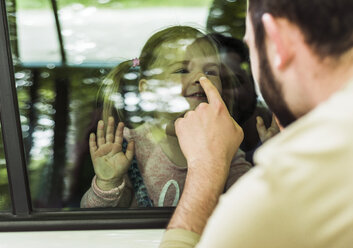 Vater berührt die Nase eines Mädchens hinter dem Autofenster - UUF004255