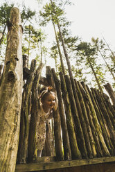 Smiling girl peeking from behind wooden fence - UUF004292