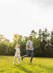 Vater und Tochter laufen mit Papierwindmühle auf Wiese - UUF004299