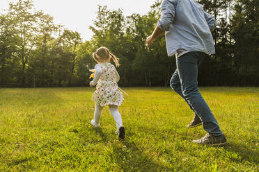 Father and daughter running with paper windmill on meadow - UUF004300