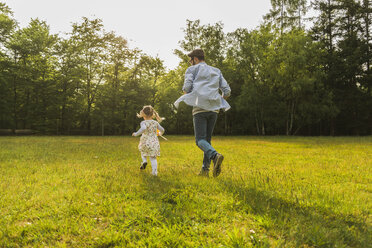 Vater und Tochter laufen mit Papierwindmühle auf Wiese - UUF004301