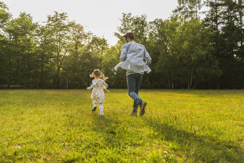 Vater und Tochter laufen mit Papierwindmühle auf Wiese - UUF004301