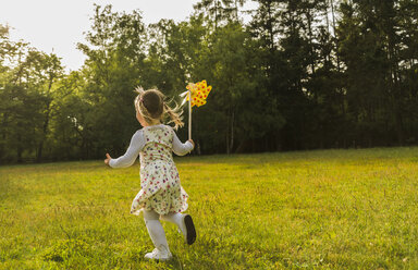 Girl running with paper windmill on meadow - UUF004302