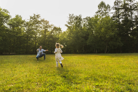 Mädchen läuft auf der Wiese dem Vater entgegen, lizenzfreies Stockfoto