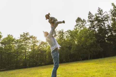 Vater hebt Tochter auf der Wiese hoch, lizenzfreies Stockfoto