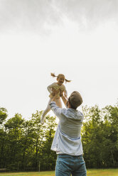 Father lifting up daughter on meadow - UUF004311