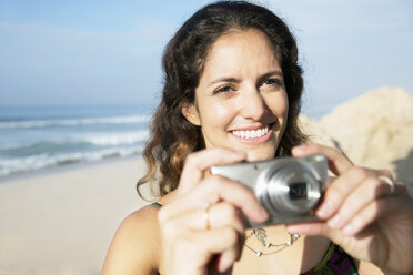 South Africa, smiling woman holding camera at the coast - TOYF000651