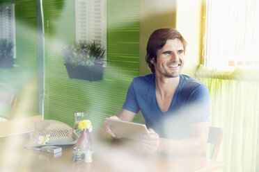 Lächelnder Mann in einem Café mit digitalem Tablet - TOYF000679